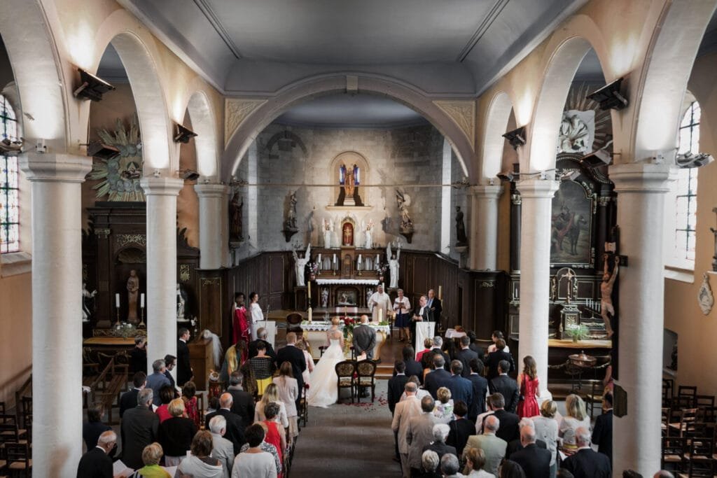 Cérémonie de mariage dans une grande église, avec un couple de mariés devant l’autel, un chœur en tenues rouges et des invités réunis pour célébrer l’union.
