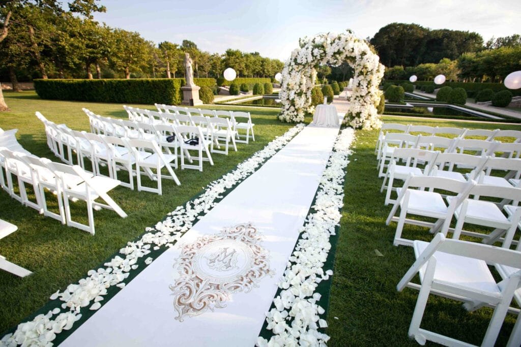 Allée de mariage élégamment décorée avec des pétales de rose et une arche florale en extérieur.