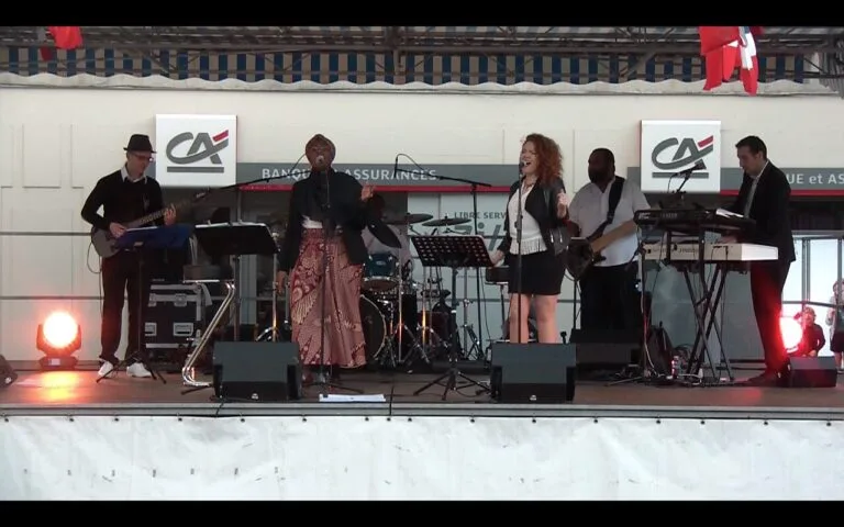 Fran's Orchestra, groupe de musique en concert en plein air avec chanteuses, guitariste, bassiste, batteur et claviériste sur scène.