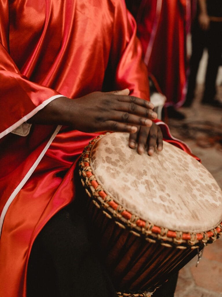 Gros plan sur les mains d’un musicien en robe rouge jouant du djembé lors d’une performance.