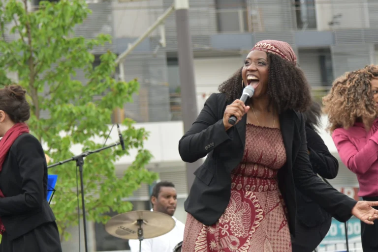 Fran Appletree, une chanteuse en tenue traditionnelle chante avec passion sur une scène en plein air, entourée de musiciens et de choristes.