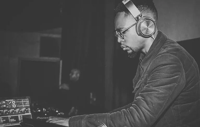 DJ concentré portant un casque audio et des lunettes, mixant de la musique sur sa console dans une ambiance sombre.