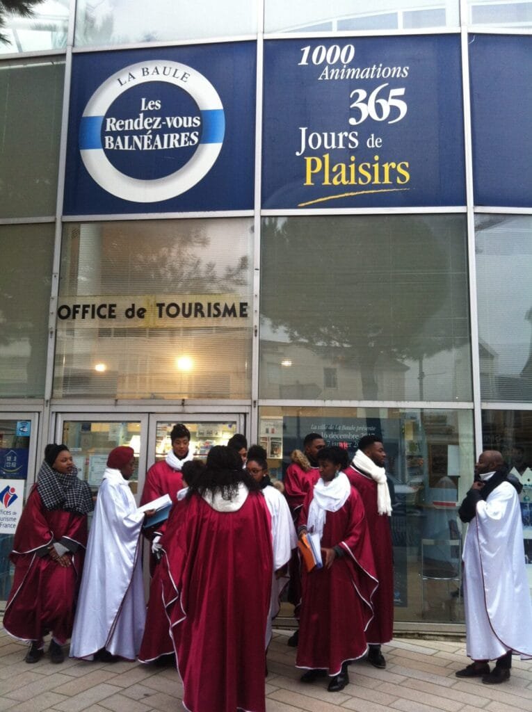 Groupe de chanteurs gospel en robes rouges et blanches réunis devant l’office de tourisme de La Baule, se préparant pour une prestation.