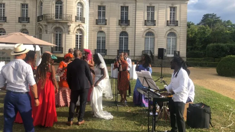 Jazz Pearl's, un groupe de musiciens et chanteurs anime une réception de mariage en plein air devant un élégant château. La mariée, en robe blanche et voile, danse avec son époux au milieu des invités vêtus de tenues colorées et raffinées.