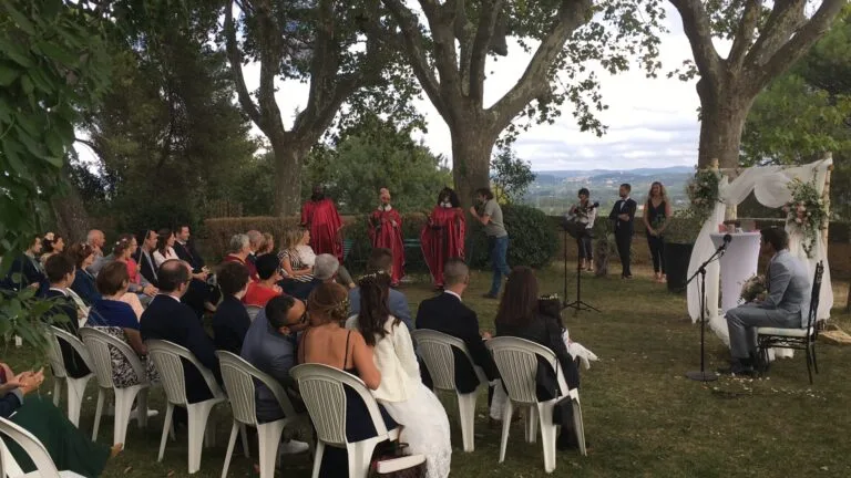 Amany, chœur gospel chantant lors d’une cérémonie de mariage en extérieur, avec les invités et le marié attentifs sous un décor naturel et une arche fleurie.