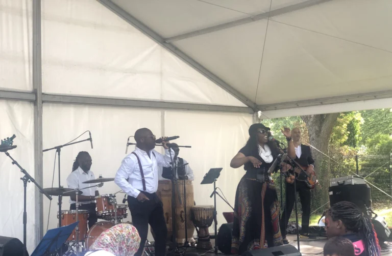 Fran's Orchestra, concert en plein air sur une place de ville avec un groupe de musiciens sur scène et un public nombreux assis à des tables ou debout.