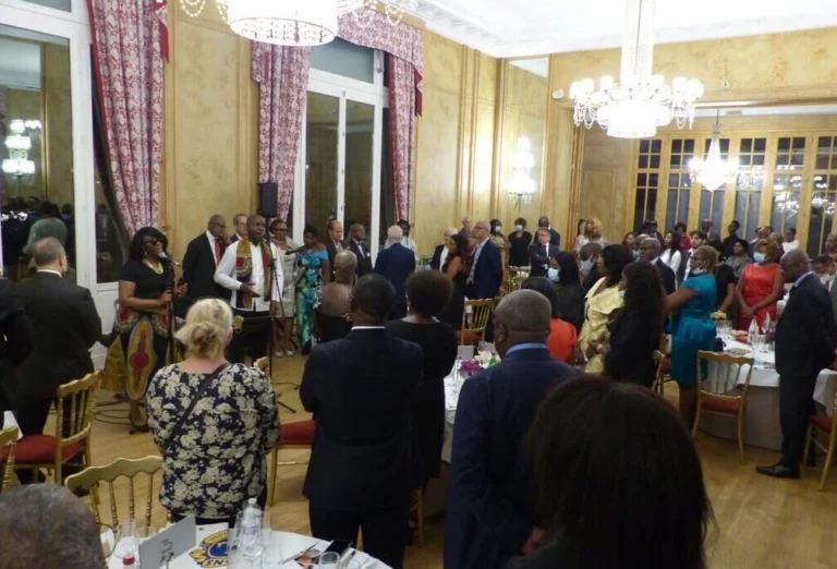 Jazz Pearl's, soirée de gala avec un chanteur et une chanteuse s’adressant à un public debout, dans une salle élégante ornée de lustres.