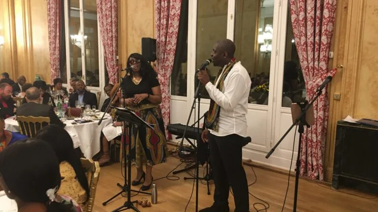 Jazz Pearl's, deux chanteurs interprétant une chanson lors d’un dîner festif dans une salle élégante, entourés d’invités attablés.