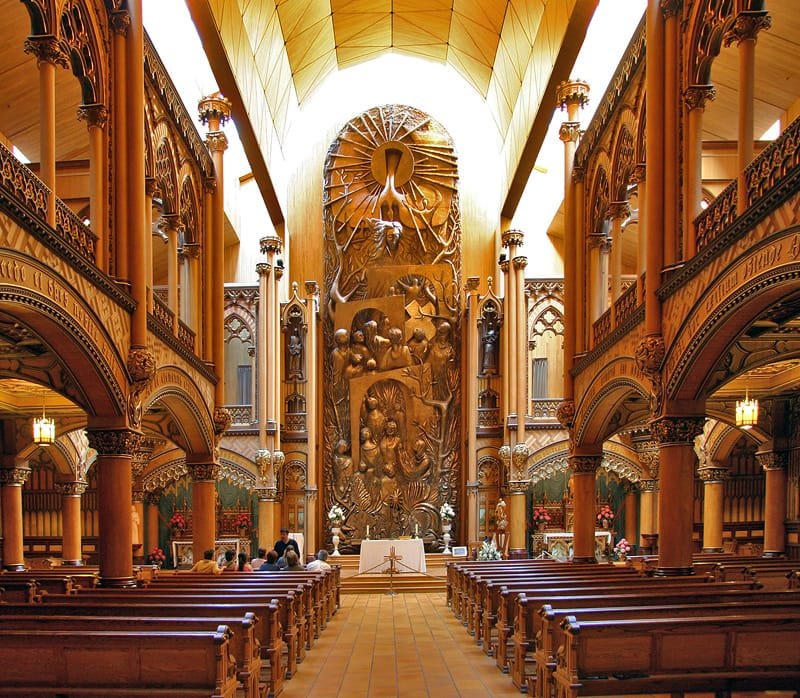 Intérieur d'une église majestueuse avec une sculpture monumentale en bois derrière l'autel.
