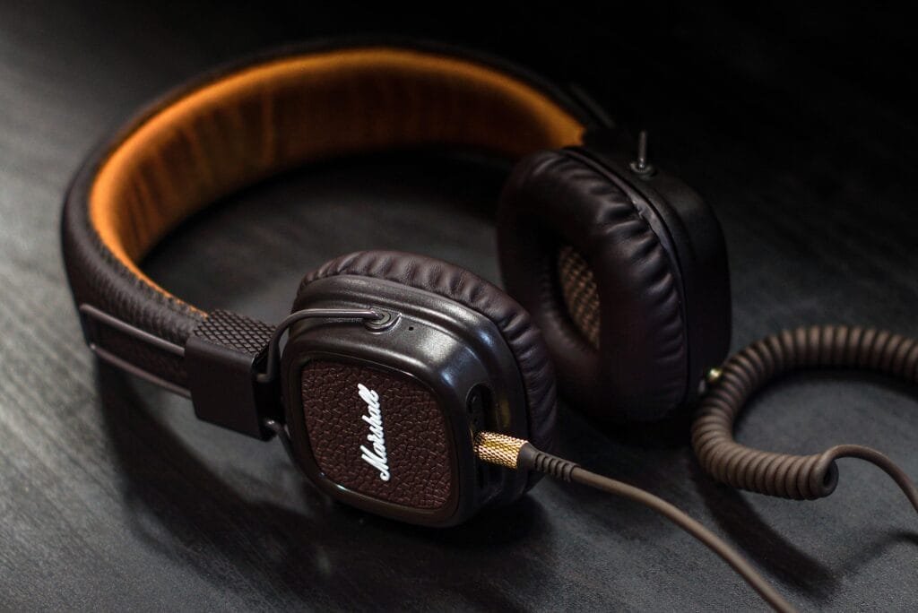 Casque audio Marshall de couleur marron avec des coussinets en cuir et un câble spiralé doré, posé sur une surface noire, offrant un design vintage et une qualité sonore premium.