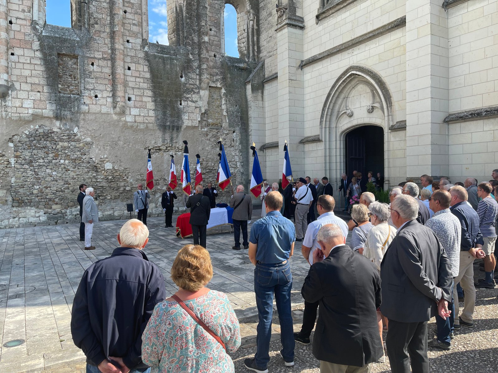 Cérémonie d’hommage funéraire devant une église avec drapeaux