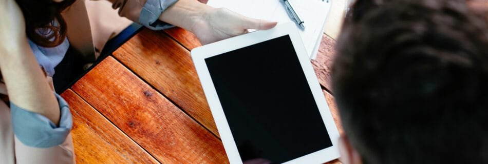 Deux collègues en réunion, utilisant une tablette numérique sur une table en bois.