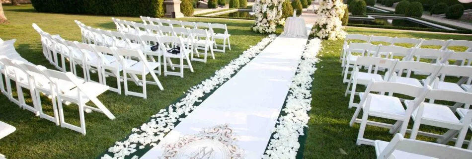 Allée de mariage décorée de pétales de roses blanches menant à une arche florale dans un jardin verdoyant.
