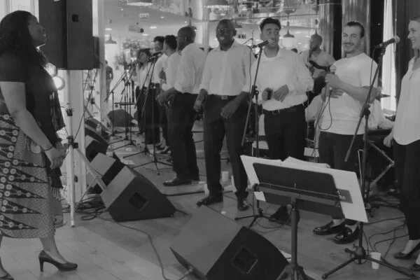 Un groupe de musiciens et chanteurs se produit sur une scène illuminée de lumières bleues, créant une ambiance immersive devant un public attentif.
