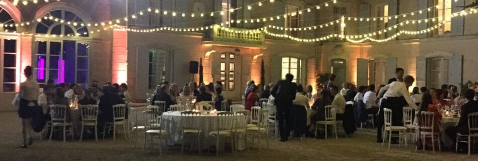 Réception nocturne en extérieur avec tables élégamment dressées, guirlandes lumineuses suspendues et un château illuminé en arrière-plan.