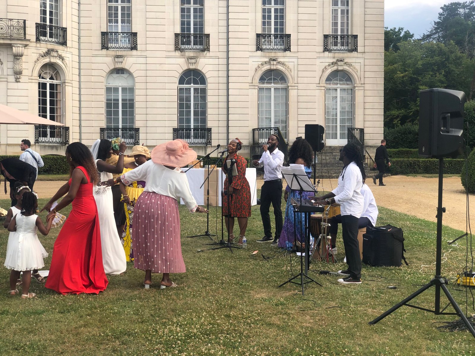 Mariage en plein air avec un groupe de musiciens et chanteurs animant la réception. La mariée en robe blanche danse entourée de ses proches vêtus de tenues colorées, tandis que les artistes chantent et jouent des instruments.
