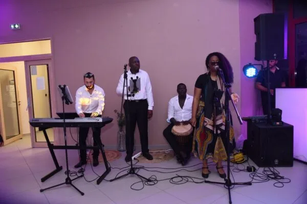 Photo d'une réception de mariage en plein air la nuit. Des invités sont rassemblés autour de tables sous une grange rustique illuminée par des guirlandes lumineuses. Les arbres en arrière-plan et la lune dans le ciel ajoutent une touche de magie à la scène.